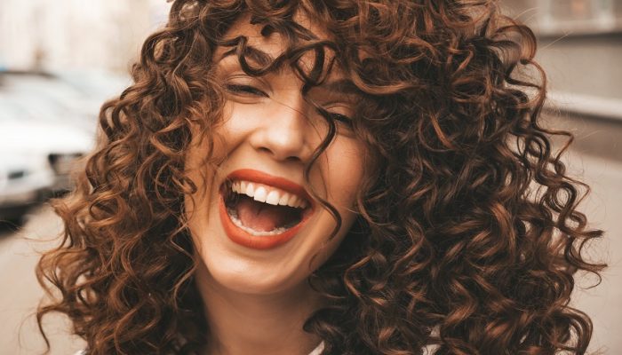 Portrait of beautiful smiling model with afro curls hairstyle.Sexy carefree girl posing in the street background.Trendy  and funny woman shows positive emotions